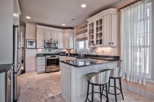 kitchen featuring stainless steel appliances, a peninsula, a sink, tasteful backsplash, and visible vents