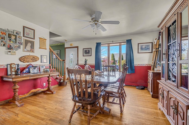 dining space with light wood-style floors, a ceiling fan, and stairs