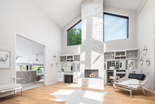 living room with a multi sided fireplace, visible vents, wood finished floors, and high vaulted ceiling