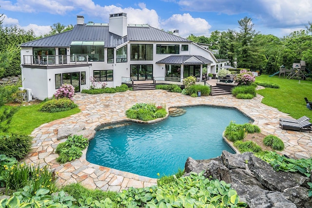 rear view of property with a chimney, a standing seam roof, stucco siding, and a patio