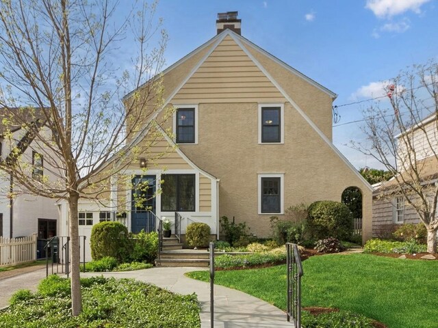 view of front of house with fence, stucco siding, a chimney, and a front lawn