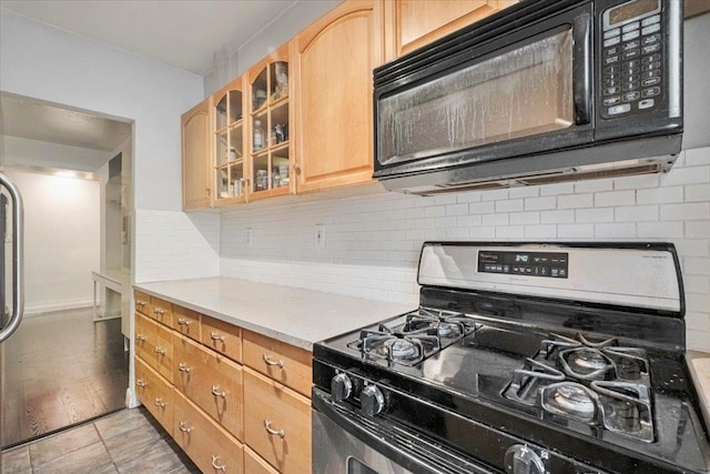 kitchen with black microwave, light countertops, gas range, backsplash, and glass insert cabinets