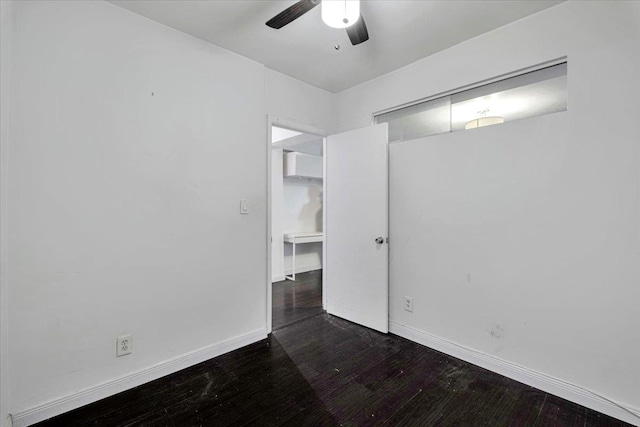 empty room featuring baseboards, dark wood-style flooring, and ceiling fan