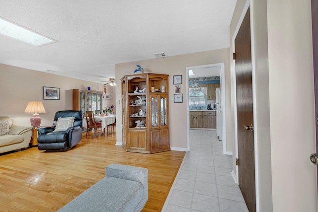 living room with visible vents, baseboards, a ceiling fan, light tile patterned floors, and a skylight