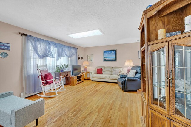 living room with light wood-style floors, a textured ceiling, and a skylight