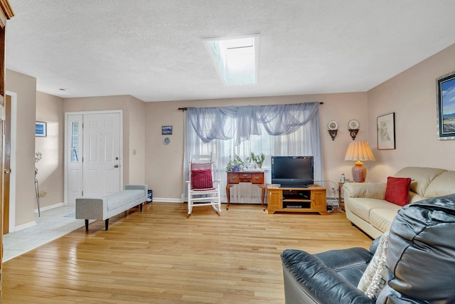 living room featuring baseboards, light wood-type flooring, a textured ceiling, a baseboard heating unit, and a skylight