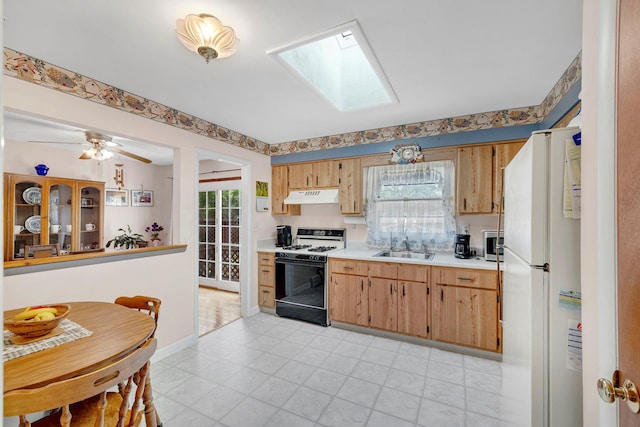 kitchen with gas range, a skylight, light countertops, freestanding refrigerator, and under cabinet range hood