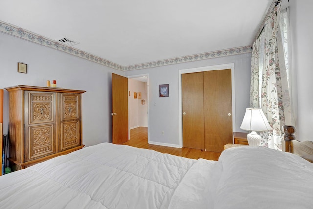 bedroom with baseboards, a closet, wood finished floors, and visible vents