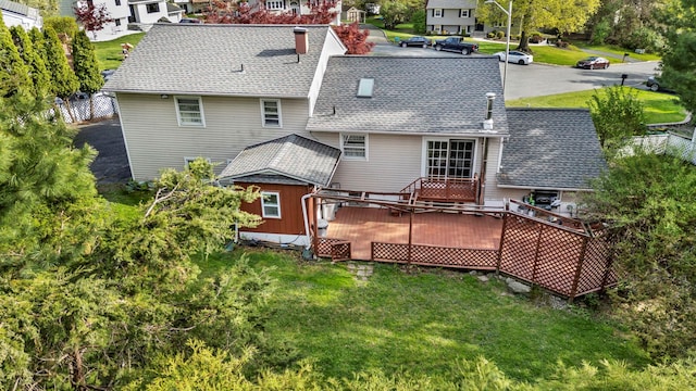 back of house featuring roof with shingles, a wooden deck, a yard, and a residential view