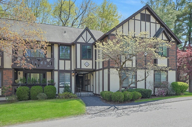 tudor home with a shingled roof, brick siding, stucco siding, and a front yard