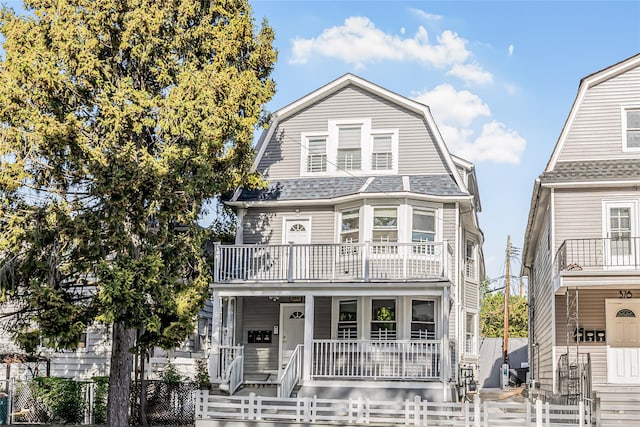colonial inspired home featuring a porch, a fenced front yard, a balcony, and a gambrel roof