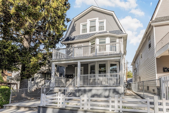 view of front facade featuring a fenced front yard, a porch, a gambrel roof, and a balcony