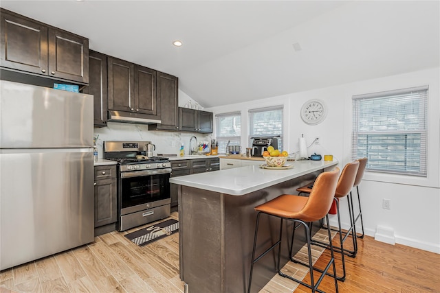 kitchen featuring dark brown cabinets, a breakfast bar, light countertops, under cabinet range hood, and stainless steel appliances