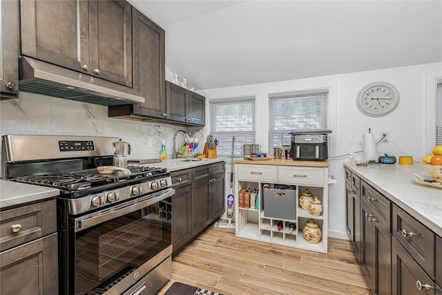 kitchen featuring dark brown cabinetry, light wood-type flooring, light countertops, under cabinet range hood, and stainless steel range with gas stovetop