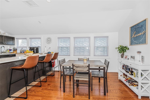 dining area featuring visible vents, baseboards, light wood finished floors, and lofted ceiling