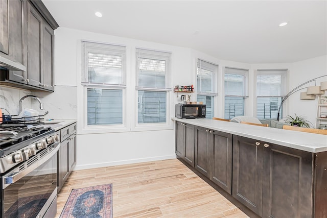 kitchen with dark brown cabinetry, black microwave, stainless steel gas range oven, light wood-style floors, and light countertops