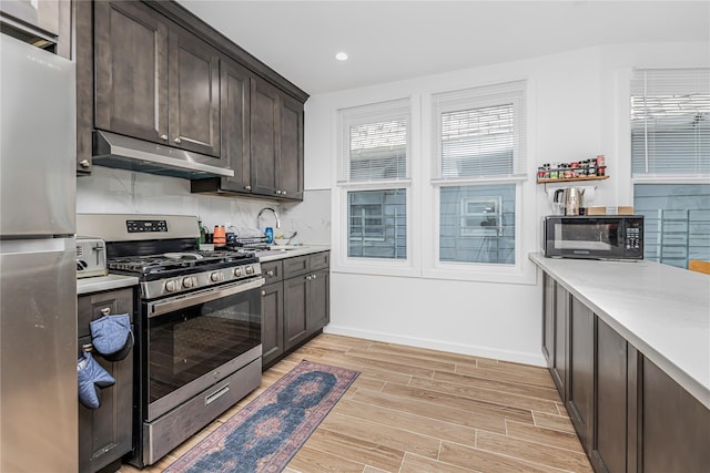 kitchen with dark brown cabinetry, light countertops, under cabinet range hood, light wood finished floors, and stainless steel appliances