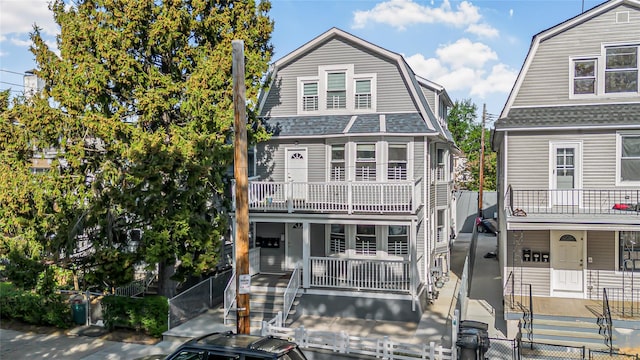 dutch colonial with covered porch, a fenced front yard, a balcony, and a gambrel roof