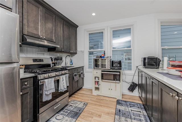 kitchen with a sink, appliances with stainless steel finishes, under cabinet range hood, and light countertops