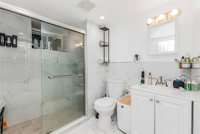 bathroom with vanity, a marble finish shower, toilet, and tile walls