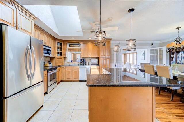 kitchen with dark stone countertops, a sink, ceiling fan, appliances with stainless steel finishes, and ornamental molding