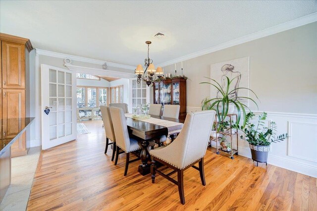 dining area with light wood-style flooring, visible vents, crown molding, and an inviting chandelier