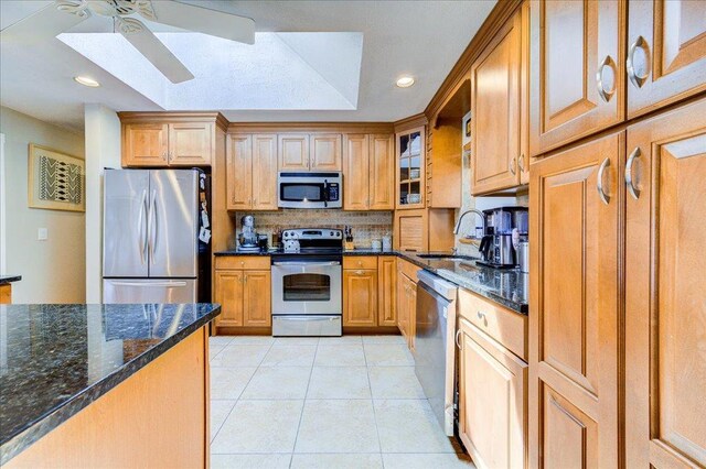 kitchen with stainless steel appliances, a sink, dark stone countertops, tasteful backsplash, and ceiling fan