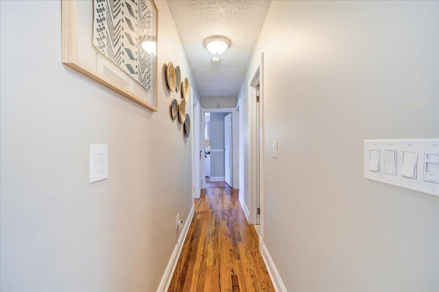 hall featuring wood finished floors, a textured ceiling, and baseboards