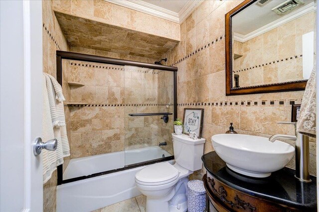 bathroom with bath / shower combo with glass door, toilet, tile walls, visible vents, and ornamental molding