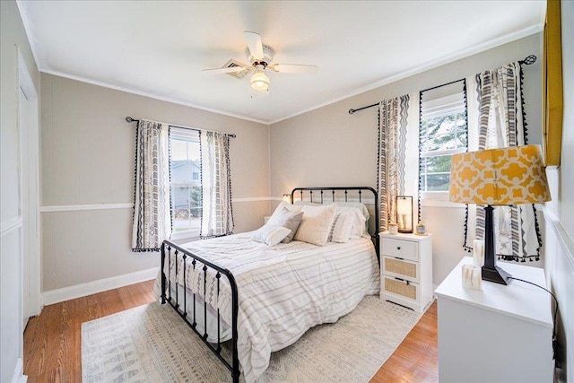 bedroom featuring light wood finished floors, ceiling fan, ornamental molding, and multiple windows