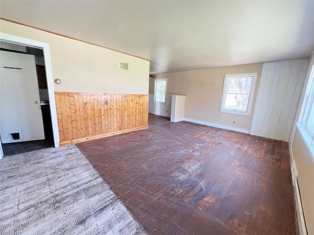 empty room featuring wood walls, wood finished floors, a wainscoted wall, and baseboards