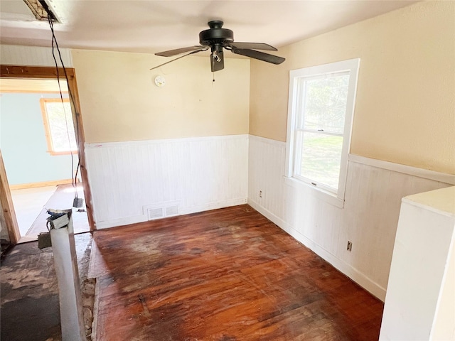 empty room with wood finished floors, visible vents, a ceiling fan, and wainscoting