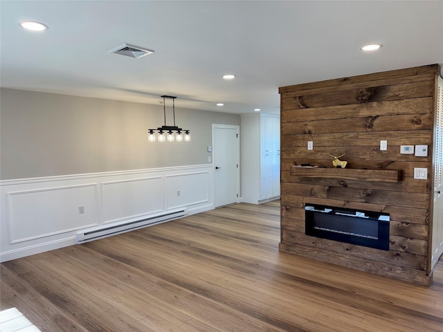 79 Enfield Ct Unit B, Ridge, NY 11961 - unfurnished living room featuring a wainscoted wall, wood finished floors, visible vents, a baseboard radiator, and a large fireplace