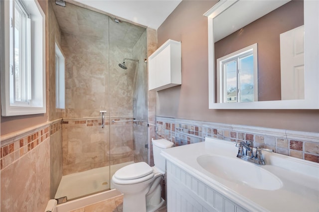 bathroom with tile walls, wainscoting, a stall shower, vanity, and toilet