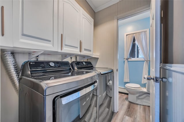 clothes washing area with washing machine and clothes dryer, crown molding, light wood-type flooring, cabinet space, and a baseboard heating unit