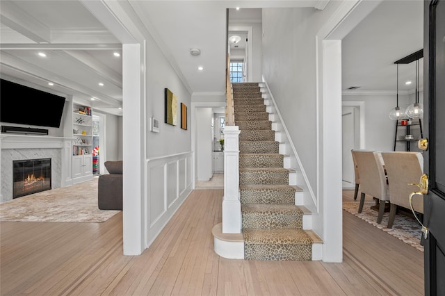 stairs with a wainscoted wall, ornamental molding, wood-type flooring, and a premium fireplace