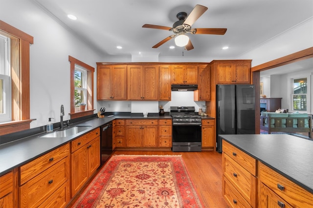 kitchen with black appliances, under cabinet range hood, a sink, dark countertops, and light wood finished floors