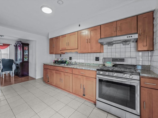 kitchen with backsplash, under cabinet range hood, brown cabinets, and stainless steel gas stove