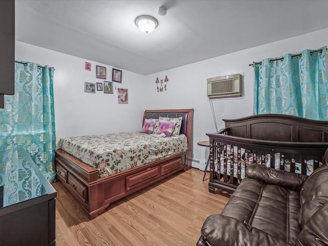bedroom with baseboard heating, a wall unit AC, and light wood-type flooring