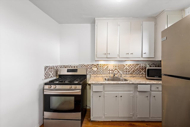 kitchen with stainless steel appliances, a sink, backsplash, wood finished floors, and light countertops