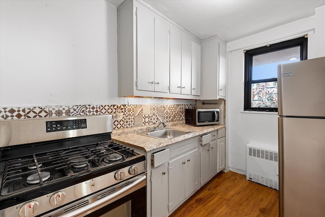kitchen with radiator, stainless steel appliances, a sink, light wood-style floors, and tasteful backsplash