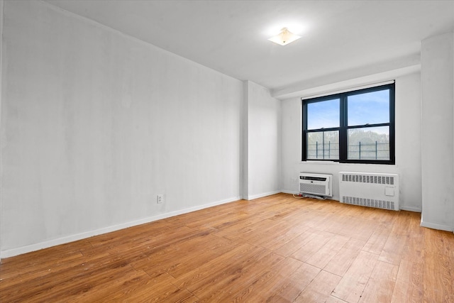 empty room featuring radiator heating unit, a wall mounted AC, baseboards, and light wood finished floors