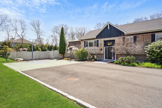 view of front of home featuring fence, basketball court, a shingled roof, and a front lawn