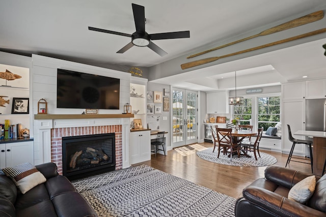living area featuring a raised ceiling, plenty of natural light, a brick fireplace, and wood finished floors