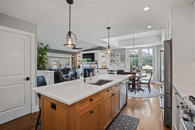 kitchen featuring appliances with stainless steel finishes, a sink, light countertops, dark wood finished floors, and brown cabinetry