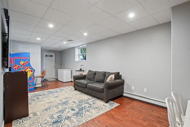 living room featuring a paneled ceiling, recessed lighting, baseboard heating, and wood finished floors