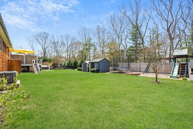view of yard featuring an outdoor structure, a fenced backyard, a playground, a trampoline, and a storage shed