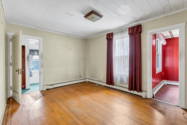 spare room featuring a baseboard heating unit, ornamental molding, hardwood / wood-style floors, and plenty of natural light