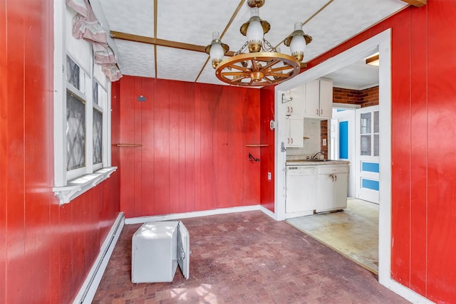 unfurnished dining area featuring baseboard heating, wood walls, an inviting chandelier, and a sink