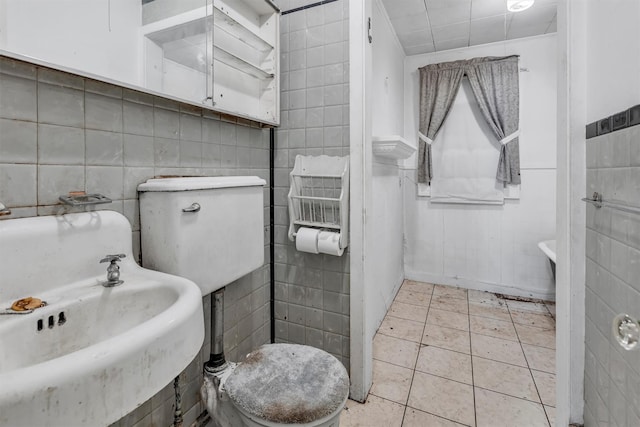 bathroom with tile walls, tile patterned floors, toilet, and a sink